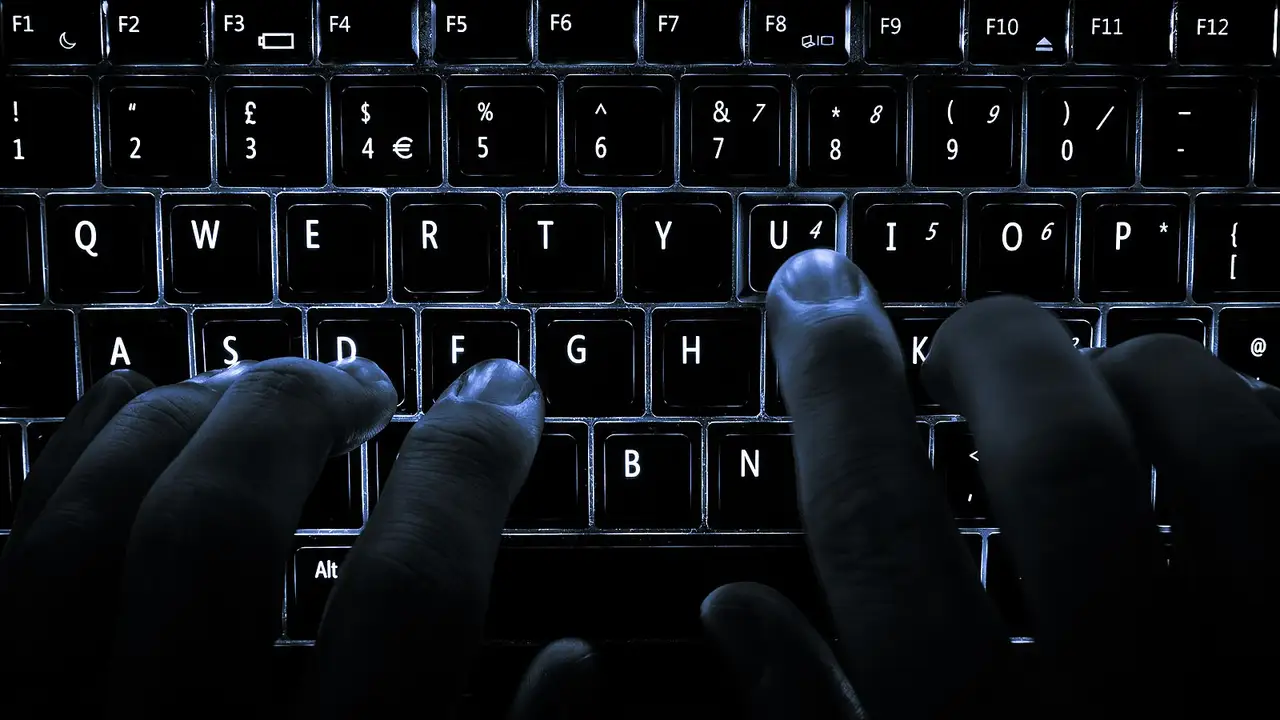 A backlit laptop computer keyboard. Most fingers are on the "home" keys for touch-typing; the 'U' key is being pressed.